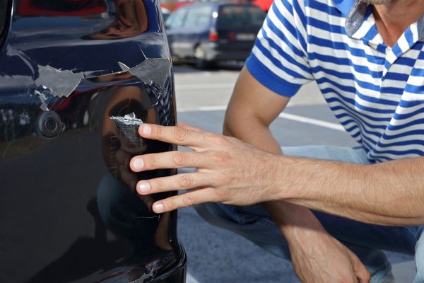 person assessing a dent and scratch on their vehicle's bumper